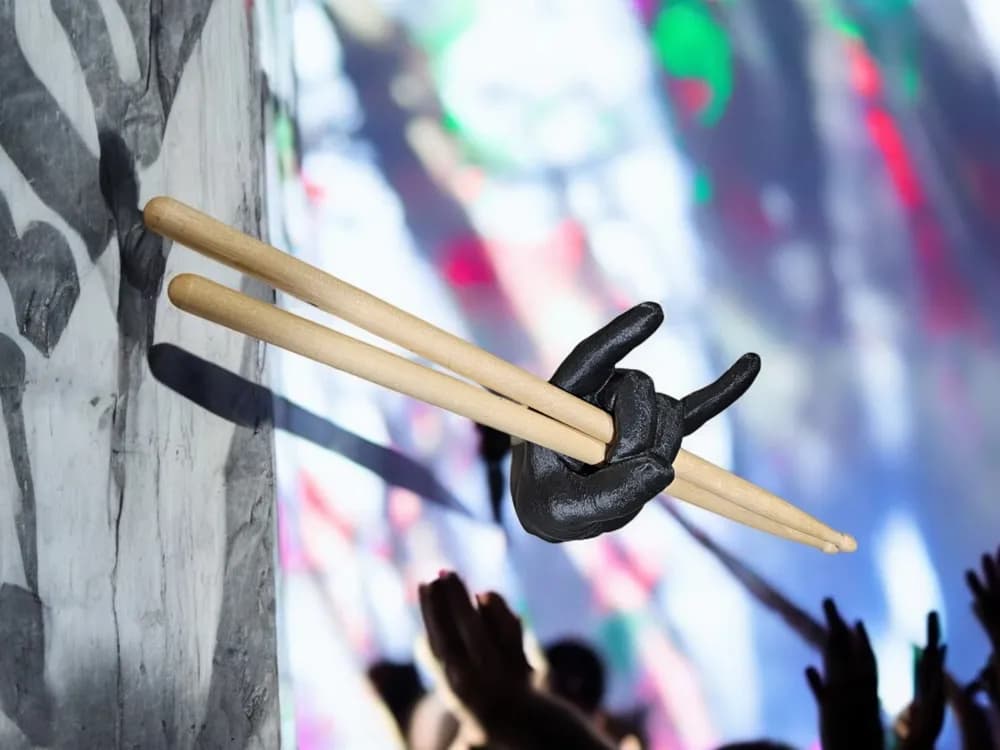 Porta-baquetas artesanal Mão do Rock montado na parede com público de show ao fundo