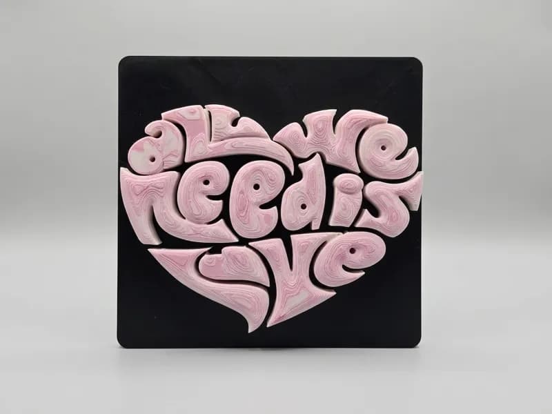 Coração Tipográfico vista frontal com detalhes das letras em relevo rosa sobre base preta